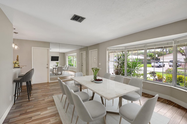 dining room with a textured ceiling, baseboards, visible vents, and light wood-style floors