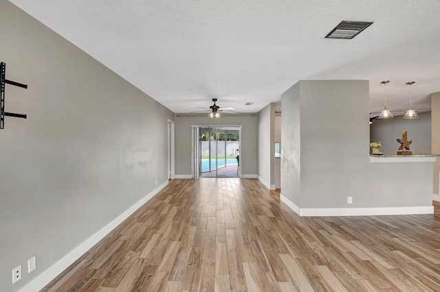 unfurnished living room with ceiling fan, wood finished floors, visible vents, and baseboards