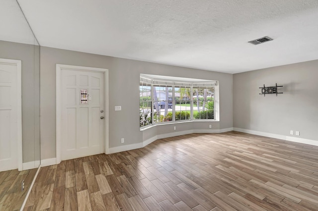 foyer entrance with visible vents, a textured ceiling, baseboards, and wood finished floors