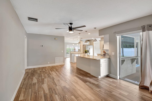 kitchen featuring light wood finished floors, stainless steel refrigerator with ice dispenser, visible vents, and white cabinetry