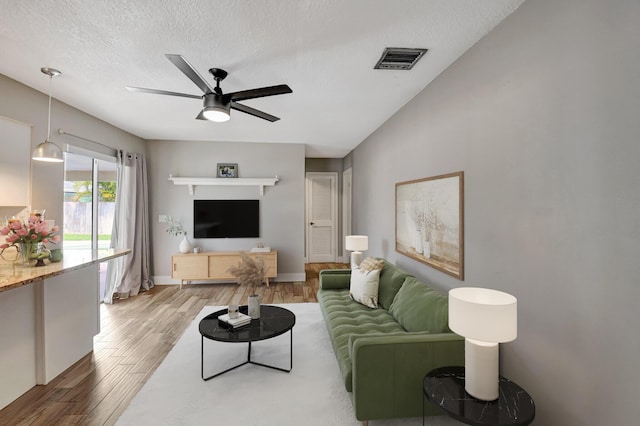 living room with light wood-type flooring, visible vents, ceiling fan, and a textured ceiling