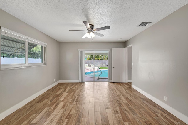 empty room featuring baseboards, wood finished floors, visible vents, and a healthy amount of sunlight