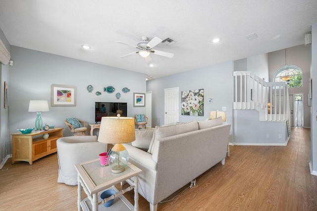 living room with light wood finished floors, baseboards, visible vents, a ceiling fan, and stairway