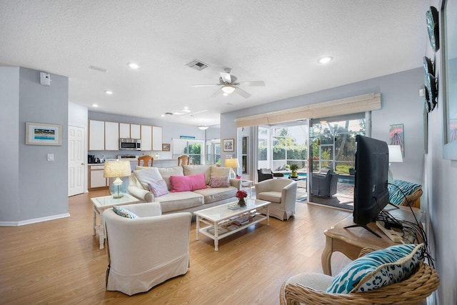 living room with light wood-type flooring, visible vents, a textured ceiling, and recessed lighting