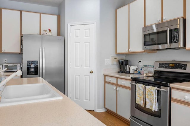 kitchen with a toaster, stainless steel appliances, a sink, white cabinetry, and light countertops