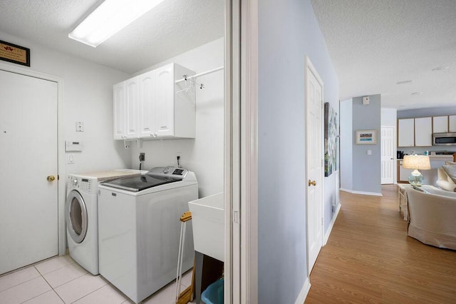 laundry room featuring a textured ceiling, light wood-type flooring, independent washer and dryer, and cabinet space