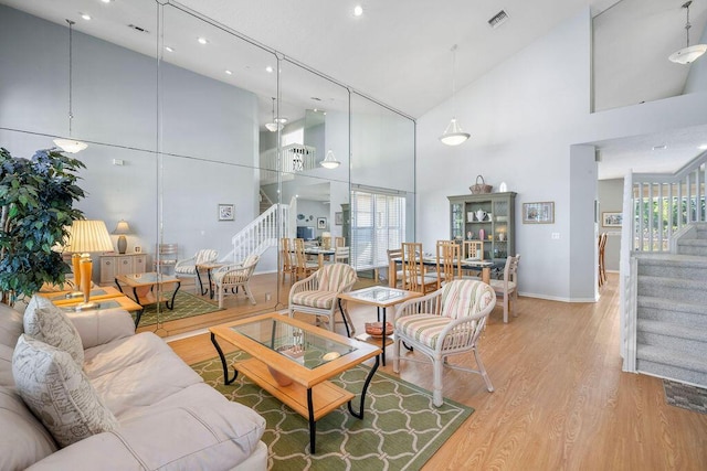 living room featuring high vaulted ceiling, stairway, visible vents, and light wood-style floors