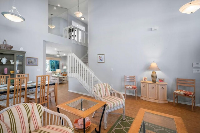 living area featuring light wood-style flooring, a high ceiling, stairway, and baseboards