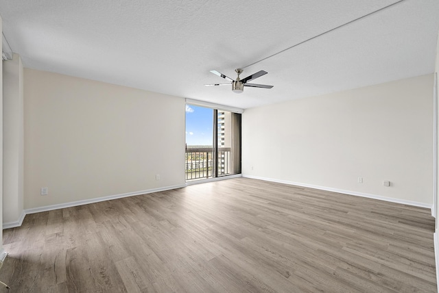 spare room featuring a wall of windows, wood finished floors, baseboards, ceiling fan, and a textured ceiling