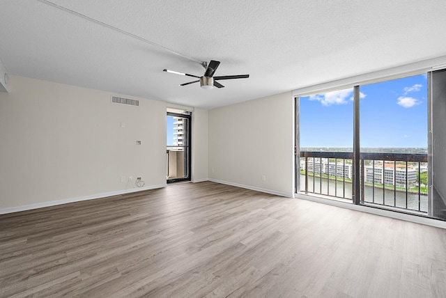 empty room with visible vents, plenty of natural light, wood finished floors, and expansive windows