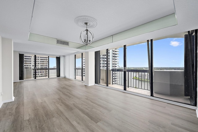 spare room with visible vents, floor to ceiling windows, an inviting chandelier, and wood finished floors