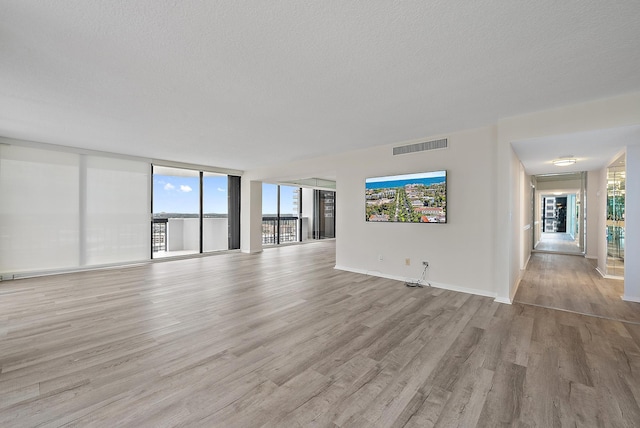 unfurnished living room with visible vents, a textured ceiling, baseboards, and wood finished floors