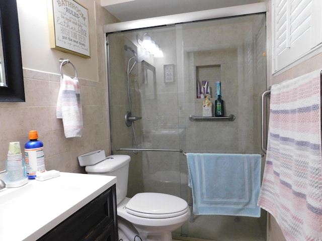 full bath with a shower with door, toilet, tile walls, and vanity