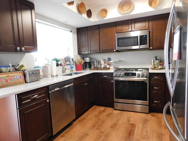 kitchen with a sink, light wood finished floors, stainless steel appliances, and light countertops