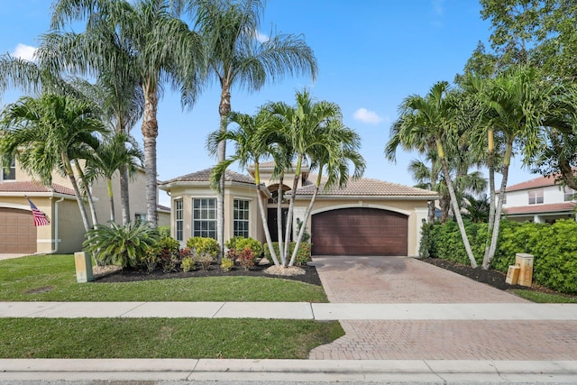 mediterranean / spanish home featuring a garage, decorative driveway, a tiled roof, and stucco siding