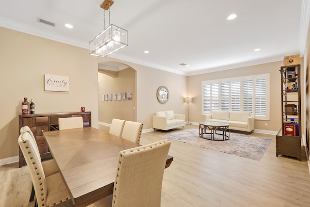 dining room featuring arched walkways, light wood-style flooring, visible vents, baseboards, and crown molding