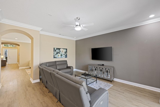 living room featuring light wood finished floors, baseboards, arched walkways, and crown molding