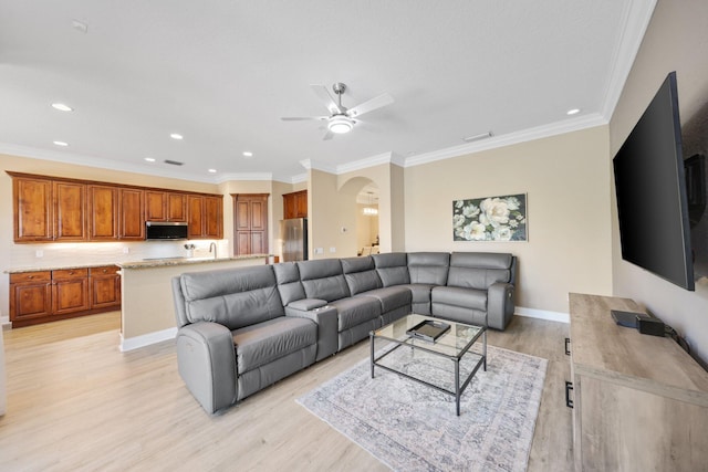 living area featuring arched walkways, light wood finished floors, ornamental molding, ceiling fan, and baseboards