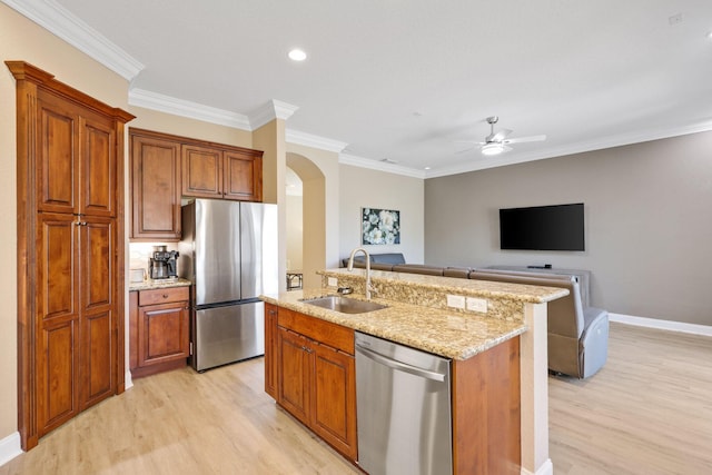 kitchen with arched walkways, an island with sink, brown cabinets, stainless steel appliances, and a sink