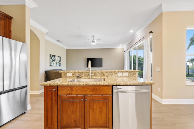 kitchen with an island with sink, brown cabinets, light stone countertops, stainless steel appliances, and a sink