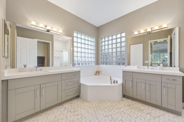 full bathroom with two vanities, a garden tub, and a sink