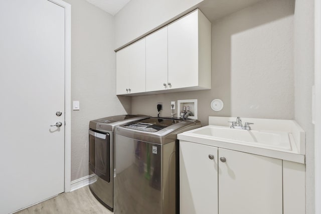 washroom with a sink, cabinet space, washing machine and dryer, and light wood-style floors