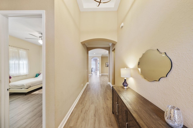 corridor with light wood-style floors, baseboards, and arched walkways