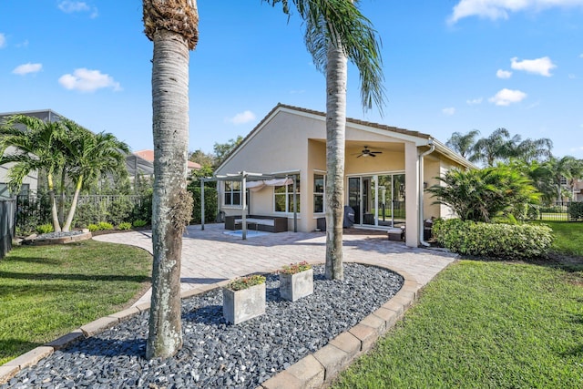 back of house with a ceiling fan, fence, a lawn, and stucco siding