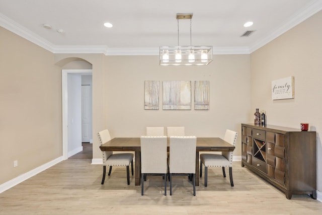 dining space featuring arched walkways, ornamental molding, baseboards, and light wood-style floors