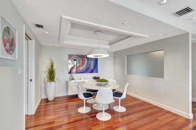 dining space featuring wood finished floors, a raised ceiling, visible vents, and baseboards