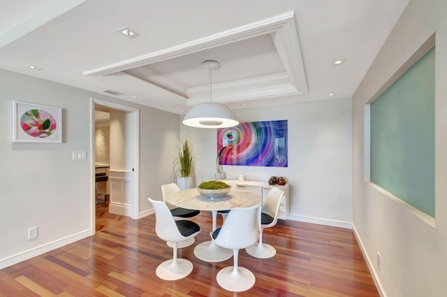 dining space with baseboards, visible vents, a raised ceiling, wood finished floors, and crown molding