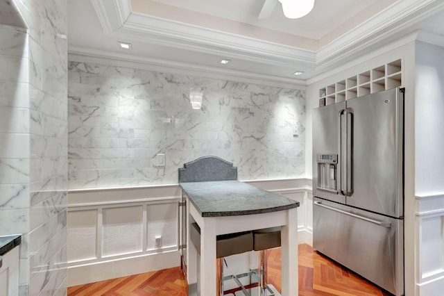 kitchen featuring dark countertops, high end refrigerator, ornamental molding, and a raised ceiling