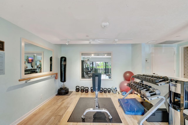 exercise room featuring baseboards, wood finished floors, and track lighting