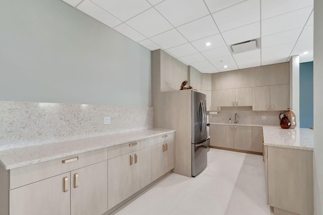 kitchen with a sink, freestanding refrigerator, light stone countertops, light floors, and tasteful backsplash