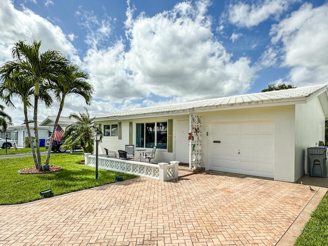 ranch-style home featuring decorative driveway, an attached garage, a front yard, and stucco siding