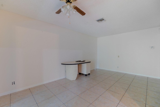 empty room featuring a textured ceiling, light tile patterned floors, visible vents, baseboards, and a ceiling fan