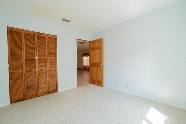 unfurnished bedroom featuring baseboards, a closet, visible vents, and light colored carpet