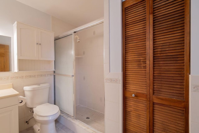 bathroom with toilet, vanity, tile walls, a closet, and a stall shower