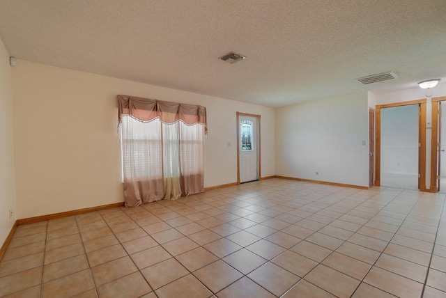 empty room with light tile patterned floors, a textured ceiling, visible vents, and baseboards