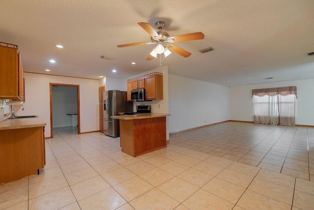 kitchen with appliances with stainless steel finishes, brown cabinets, open floor plan, a peninsula, and light countertops