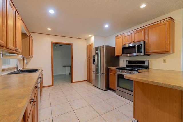 kitchen with a textured ceiling, a sink, light countertops, appliances with stainless steel finishes, and brown cabinetry