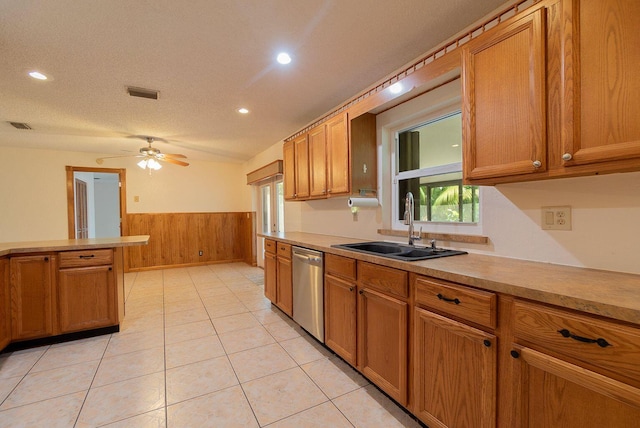 kitchen featuring light countertops, stainless steel dishwasher, wainscoting, and a sink