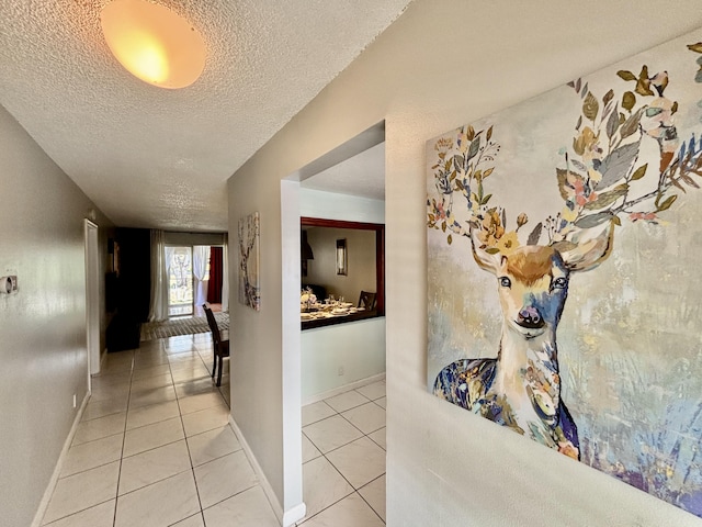 hallway with a textured ceiling, baseboards, and light tile patterned floors