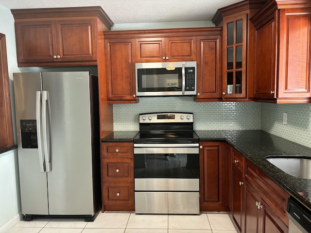 kitchen with stainless steel appliances, a sink, decorative backsplash, dark stone counters, and glass insert cabinets