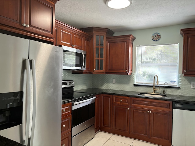 kitchen featuring light tile patterned floors, a sink, appliances with stainless steel finishes, decorative backsplash, and glass insert cabinets