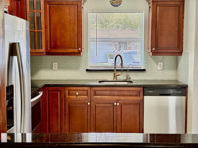 kitchen featuring stainless steel appliances, a sink, backsplash, dark stone countertops, and glass insert cabinets