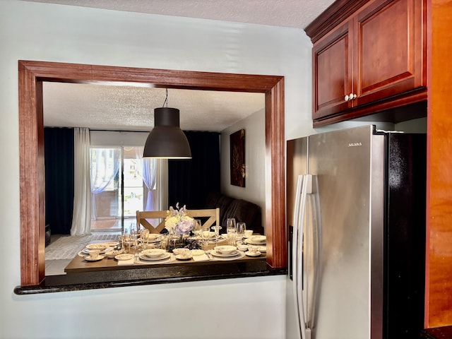 interior details with reddish brown cabinets, dark countertops, a textured ceiling, and stainless steel fridge with ice dispenser