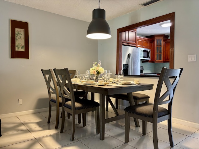 dining area featuring light tile patterned floors, visible vents, baseboards, and a textured ceiling