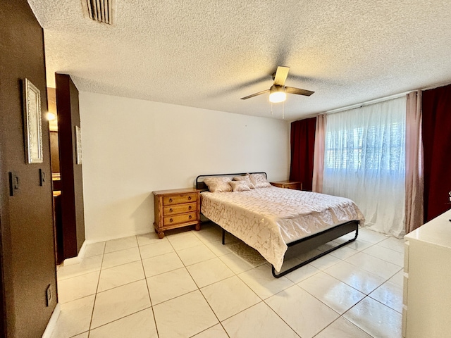 bedroom featuring light tile patterned floors, ceiling fan, visible vents, and a textured ceiling