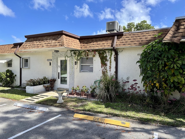 view of front facade with uncovered parking, mansard roof, a shingled roof, and cooling unit